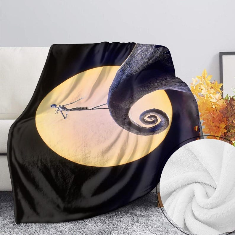 May include: A black and white throw blanket featuring a scene from The Nightmare Before Christmas. The design includes Jack Skellington in front of a full moon and a swirling, dark shape. The blanket has a soft, plush texture.
