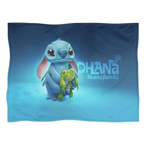 Pode incluir: Um cobertor azul com uma ilustra&ccedil;&atilde;o de desenho animado de Stitch de Lilo & Stitch segurando um sapo verde. O texto "OHANA Means family" est&aacute; em branco. O fundo &eacute; um gradiente azul.