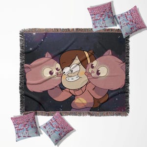 Könnte beinhalten: Eine gewebte Decke und vier Kissen. Die Decke zeigt ein Cartoon-Bild eines Mädchens mit zwei rosa katzenartigen Kreaturen vor einem Sternenhintergrund. Die Kissen haben ein rosa Flamingomuster auf blauem Hintergrund.