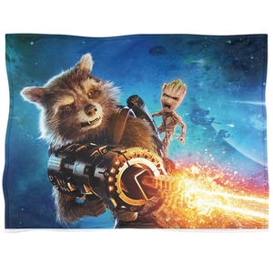 May include: A plush blanket featuring Rocket Raccoon wielding a large weapon, with Groot standing beside him. The background depicts a space scene with planets and spacecraft. The blanket has a blue and green color scheme.