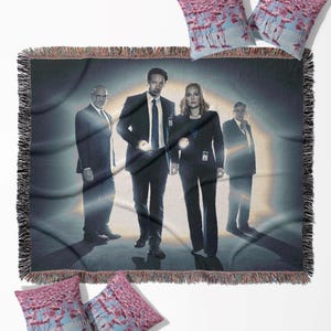 May include: A woven throw blanket and four throw pillows. The blanket features a group of people in suits. The pillows have a pink flamingo design. The blanket has a black fringe.