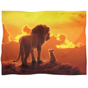 Puede incluir: Una manta rectangular con un león y un cachorro contra un atardecer naranja y amarillo. La imagen es de una popular película de animación, con el león de pie y el cachorro sentado.