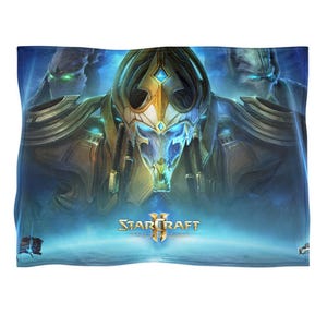 Op de afbeelding: Een blauwe deken met een gedetailleerde illustratie van personages uit de videogame StarCraft II. De centrale figuur is een robot met gouden en blauwe accenten, omringd door andere figuren en het logo van de game.