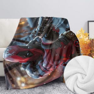 May include: A soft blanket displaying a detailed image of a character in a red and black suit, holding a weapon. The blanket has a white, fluffy texture on the reverse side, and is draped over a white sofa.