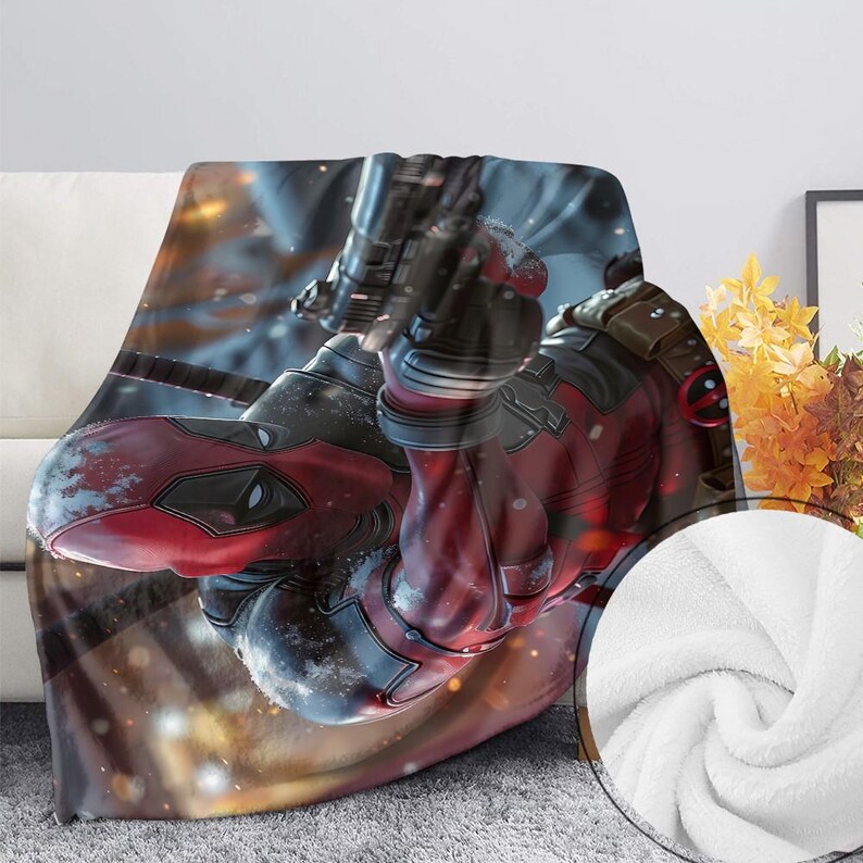 May include: A soft blanket displaying a detailed image of a character in a red and black suit, holding a weapon. The blanket has a white, fluffy texture on the reverse side, and is draped over a white sofa.