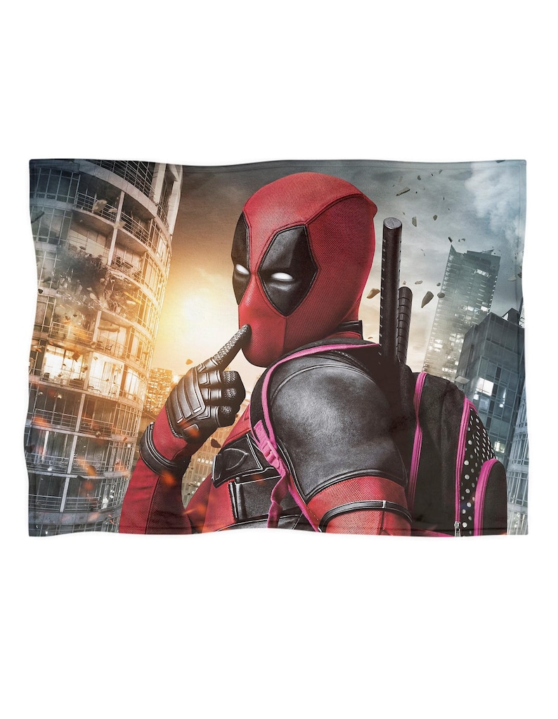 May include: A red and black Deadpool blanket featuring the character in his signature mask and costume, with a cityscape background. The blanket showcases the superhero in a dynamic pose, with a finger to his lips.