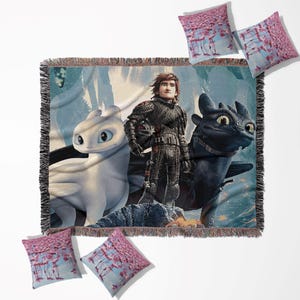 Puede incluir: Una manta tejida y cuatro cojines con personajes de la película animada "Cómo entrenar a tu dragón". La manta representa a Hipo, Desdentado y Furia Luminosa. Los cojines tienen un diseño rosa y azul.