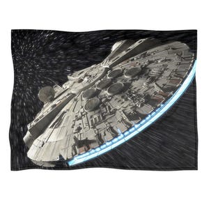 Könnte beinhalten: Eine Decke mit einem detaillierten Bild des Raumschiffs Millennium Falcon im Weltraum. Das Schiff ist grau mit komplizierten Details und einem blau leuchtenden Rand. Der Hintergrund zeigt eine schwarze Weltraumszene mit weißen Lichtstreifen.