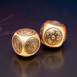 以下が含まれることがあります： 金色の球状のサイコロ2つ。複雑な彫刻が施されており、片方には漢字と陰陽のシンボル、もう片方には龍のモチーフが描かれています。サイコロは暗い背景に配置されています。