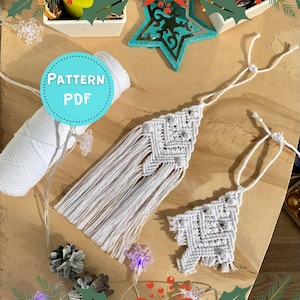 May include: Two white macrame Christmas tree ornaments with fringe, displayed on a wooden surface. A spool of white string and a teal circle with the text "PATTERN PDF" are also visible. Decorative lights and pinecones add to the festive theme.