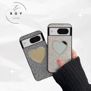 May include: Two phone cases with a sparkling, glittery design. One case has a gold heart cutout, and the other has a silver heart cutout. The cases are black around the camera and have the text "ROY CASE" in a circle.