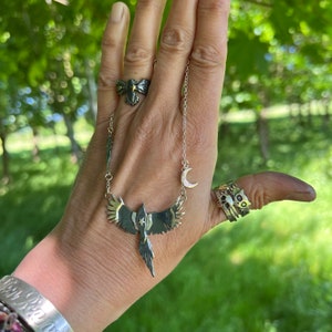 K&ouml;nnte beinhalten: Eine silberne Halskette mit einem Vogelanh&auml;nger, einem Mondsichel-Anh&auml;nger und zwei Ringen. Der Vogelanh&auml;nger hat goldfarbene Fl&uuml;gel. Ein Ring hat ein Schleifendesign mit einem goldenen Stern. Der andere Ring hat ein Katzen-Design.
