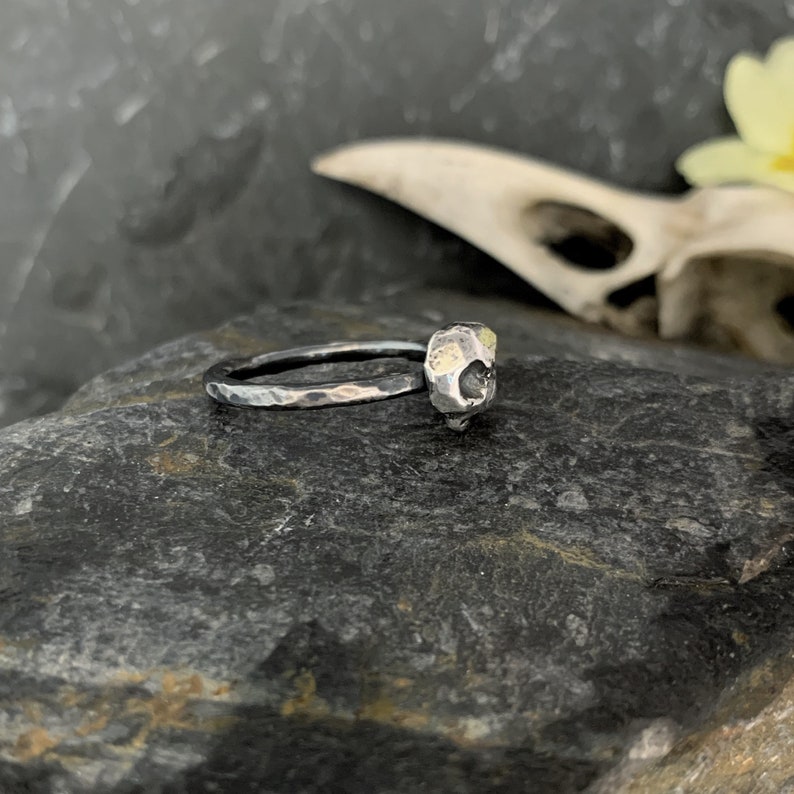 May include: A silver ring with a textured skull-shaped band. The skull is accented with small gold details.