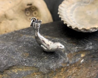 May include: A silver charm of a seal in a diving pose. The charm is detailed with a textured surface and a loop for attaching to a necklace or bracelet.