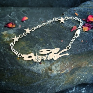 May include: A silver bracelet featuring a cut-out design of a running hare and five star charms. The bracelet is displayed on a dark grey textured surface.