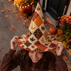 May include: A quilted witch hat featuring a patchwork design of orange, brown, and cream fabric squares. The pattern includes illustrations of pumpkins, black cats, bats, moons, and autumn leaves, all stitched together in a tall, pointed cone shape.