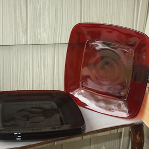 May include: Three square glass plates, two are red and one is black. The plates are stacked on top of each other.