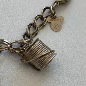 Puede incluir: Pulsera de abalorios plateada con un dije en forma de carrete y una etiqueta de Mickey Mouse. El dije de carrete est&aacute; detallado con l&iacute;neas de hilo enrolladas. La etiqueta de Disney muestra el nombre y el logotipo de Disney.