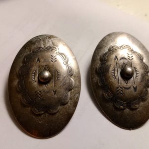 May include: Pair of vintage silver-toned oval earrings. Each earring features a central raised bead surrounded by etched geometric and floral patterns. The earrings have a tarnished, aged appearance, suggesting they are antique or vintage.