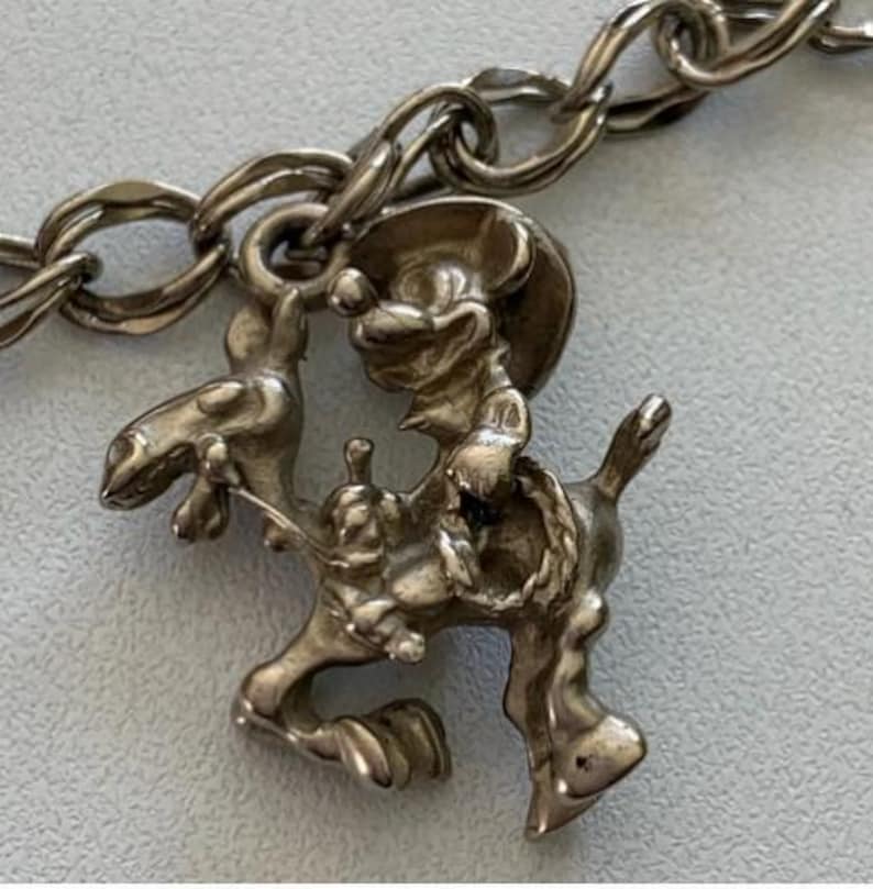 Puede incluir: Un eslab&oacute;n de pulsera con dije plateado que representa a un rat&oacute;n vaquero montando a caballo. El dije est&aacute; detallado con un sombrero de vaquero y una cuerda, sujeto a una cadena plateada. El dise&ntilde;o es de estilo vintage.