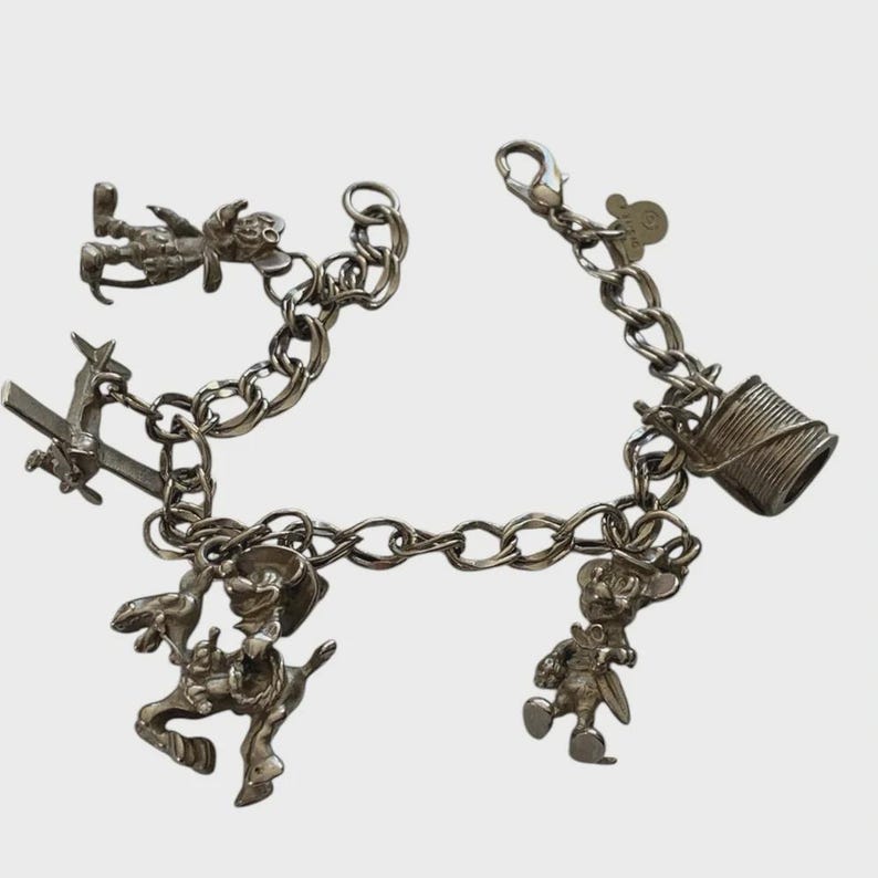 Puede incluir: Una pulsera de plata con varios dijes detallados. Los dijes incluyen un vaquero a caballo, un personaje en un avi&oacute;n, un personaje con un tambor y otras figuras de dibujos animados. La pulsera tiene un cierre de langosta.