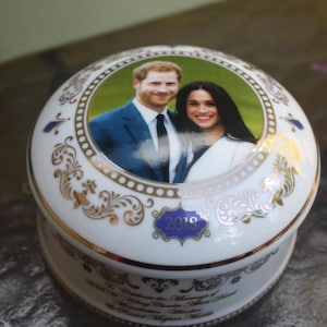 May include: A white porcelain trinket box with a gold rim and decorative floral patterns. The lid features a color photograph of a couple. The year "2019" is displayed on the front in a blue banner.