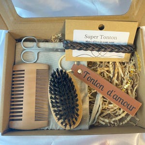 Peut inclure: Coffret cadeau de soins pour homme. Il comprend un peigne en bois, une brosse à barbe, des ciseaux, un bracelet en cuir tressé, un porte-clés et une étiquette en cuir avec le texte "Tonton d'amour". Une carte avec le texte "Super Tonton" est également incluse.