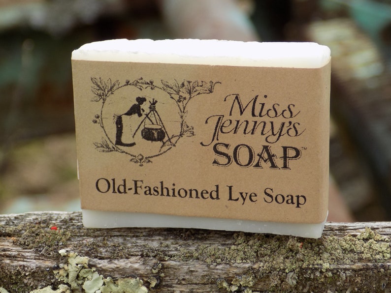 May include: A bar of white lye soap with a brown paper label. The label has a black and white illustration of a woman making soap and the text "Miss Jenny's SOAP" and "Old-Fashioned Lye Soap".