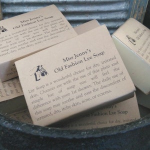 May include: A close-up of several brown cardboard boxes of Miss Jenny's Old Fashion Lye Soap. The boxes are stacked in a black cauldron. The soap is described as a wonderful choice for dry, irritated skin. The text on the boxes reads: "Lye Soap is a wonderful choice for dry, irritated skin. Chances are with the use of this plain and simple bar of soap you will feel the difference with your 1st shower. The daily use of this soap may soothe and ease the discomfort of irritated, dry, itchy skin, acne, or eczema."
