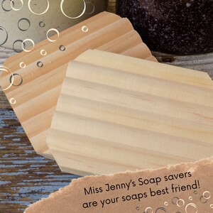 May include: Two wooden soap savers, one with a smooth surface and the other with ridges. The savers are made of light brown wood and are sitting on a blue and white wooden surface. The text "Miss Jenny's Soap savers are your soaps best friend!" is written on a piece of brown paper.