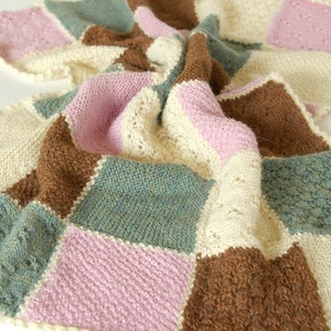 Può includere: Una copertina per neonati a maglia con un design a patchwork in tonalità di marrone, rosa e verde. La copertina è realizzata in filato morbido e ha una texture delicata.