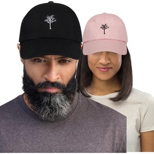 Può includere: Due cappellini da baseball, uno nero e uno rosa, ciascuno con un logo di albero bianco ricamato sul davanti. Il cappellino nero è indossato da una persona con la barba, e il cappellino rosa è indossato da una persona con i capelli scuri.