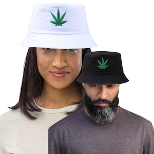 May include: Two bucket hats, one white and one black, each embroidered with a green cannabis leaf. The hats are shown on two people, a woman and a man, against a white background. The hats are a casual accessory.