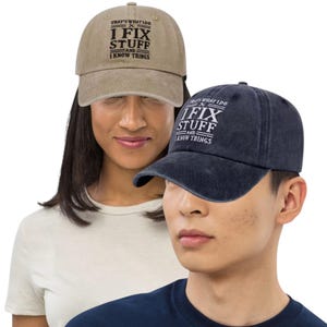 May include: Two baseball caps, one tan and one navy blue, with the text "THAT'S WHAT I DO, I FIX STUFF AND I KNOW THINGS" printed in white. The caps have a curved brim and an adjustable strap.