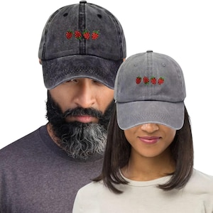 May include: Two baseball caps, one dark gray and one light gray, each embroidered with three red strawberries. The caps have a vintage, worn look. The caps are a casual accessory.