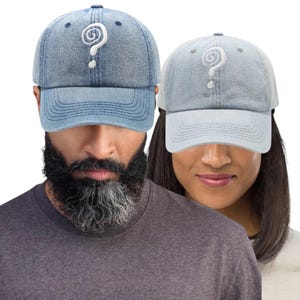 May include: Two denim baseball caps, one light blue and one faded blue, each embroidered with a white question mark. The caps have a curved brim and adjustable strap. The caps are a unisex accessory.