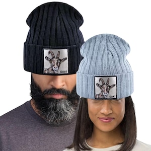 Pode incluir: Duas toucas de malha canelada, uma preta e outra azul clara. Cada touca apresenta um patch retangular com uma ilustração de cabra e a palavra "GOAT". As toucas são um acessório casual.