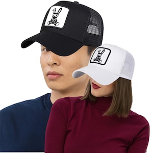 May include: Two baseball caps, one black and one white, each featuring a square patch with a cartoon bunny design. The black cap has a mesh back. The white cap also has a mesh back. Both caps have a curved brim.