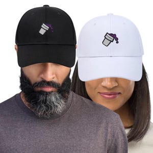 May include: Black and white baseball caps featuring an embroidered cup design with purple liquid. The caps have a classic six-panel design, curved peak, and an adjustable strap for a comfortable fit.