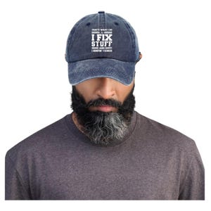Könnte beinhalten: Denimblaue Baseballkappe mit weißem Text "THAT'S WHAT I DO I FIX STUFF AND I KNOW THINGS". Die Kappe hat einen gebogenen Schirm und einen verstellbaren Riemen.