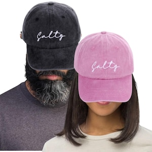 Peut inclure: Deux casquettes de baseball, une noire et une rose, avec le mot "Salty" brodé en blanc. Les casquettes sont en matière douce et texturée, avec un design classique et ajustable.