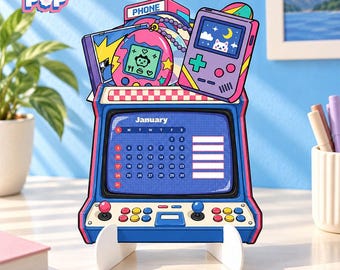May include: A desk calendar shaped like a retro arcade machine with a blue frame, featuring a January grid on the screen. The top displays a pink digital pet, a purple handheld game console, and a phone sign. The logo FLOGI POP is visible.