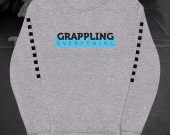 Puede incluir: Una sudadera gris jaspeada con el texto "GRAPPLING EVERYTHING" en negro y azul. Las mangas tienen una serie de acentos cuadrados negros. La sudadera es de cuello redondo.