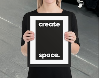 Puede incluir: Impresión artística enmarcada en negro con las palabras "create space." en blanco. La obra de arte tiene un fondo negro con un borde blanco. La impresión la sostiene una persona que lleva una camiseta negra.