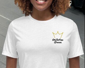 Puede incluir: Camiseta blanca con un diseño de corona dorada y la frase "Guillotine Queen" en negro. La camiseta de manga corta está hecha de un material suave.