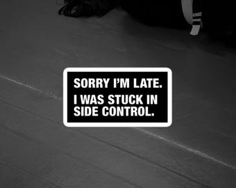 May include: A rectangular sticker with a black background and a white border. The text in white capital letters reads: SORRY I'M LATE. I WAS STUCK IN SIDE CONTROL. The sticker is positioned over a black and white image of a person in a martial arts uniform.