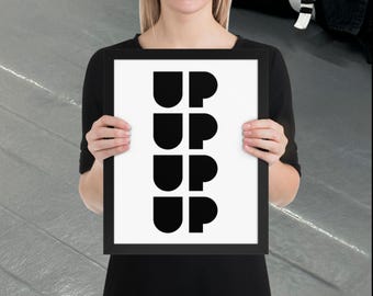 Puede incluir: Una impresión artística enmarcada con la palabra "UP" repetida cuatro veces en un diseño minimalista negro y audaz. La obra de arte se muestra sobre un fondo blanco dentro de un marco negro. La impresión la sostiene una persona con una parte superior negra.
