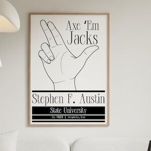 以下が含まれることがあります： 「Axe 'Em Jacks」と「Stephen F. Austin State University」の文字が入った、額縁に入った白黒ポスター。ポスターには手のジェスチャーが描かれています。ポスターはリビングルームに飾られています。