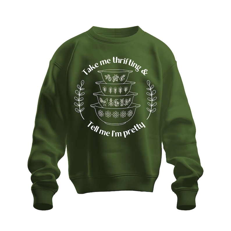 Puede incluir: Una sudadera verde oscuro con el texto "Take me thrifting & Tell me I'm pretty" en blanco. El gr&aacute;fico presenta una pila de cuencos vintage. El dise&ntilde;o est&aacute; rodeado por una guirnalda floral blanca.
