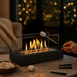 May include: A black tabletop fireplace with a glass shield, flames, and a person roasting a marshmallow. A bowl of marshmallows and roasting forks are nearby. The scene is set indoors with soft lighting.